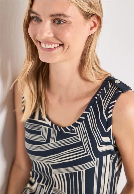 Lächelnde Frau mit blondem Haar trägt ein ärmelloses Top mit schwarz-weißem geometrischem Muster.