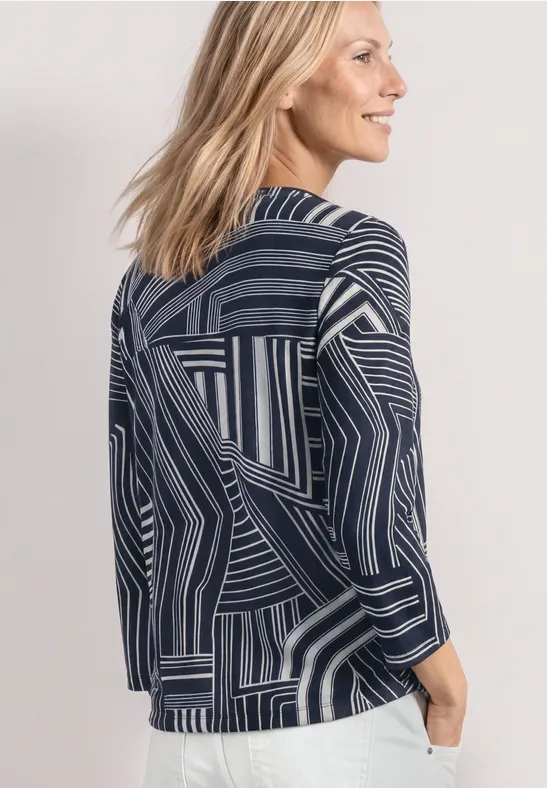Drei-Viertel-Ansicht einer Frau mit blondem Haar in einer geometrisch gemusterten dunkelblauen Jacke.