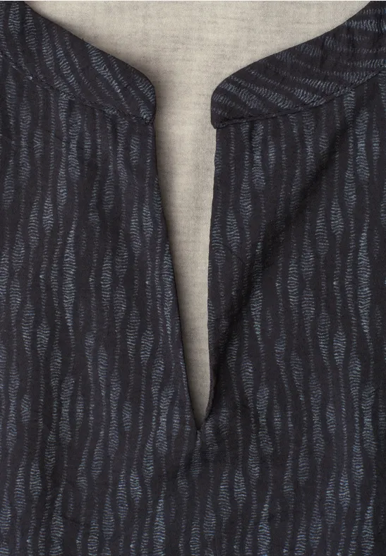 Dunkles Shirt mit blauem Wellenmuster und V-förmigem Kragen auf hellem Stoffhintergrund.