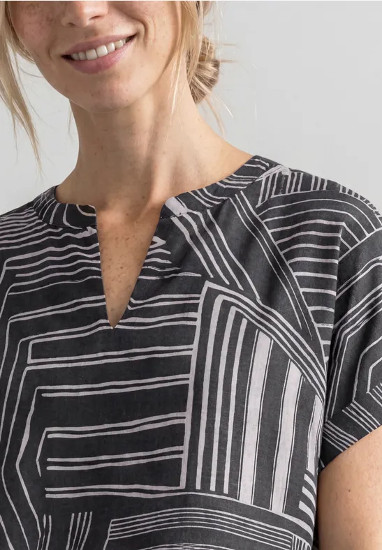 Frau im Schwarz-Weiß-Shirt mit geometrischem Linienmuster und leichtem Lächeln.