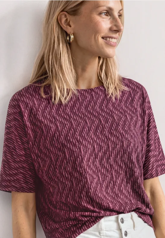 Une personne porte un t-shirt à manches courtes violet à motifs et un pantalon blanc.