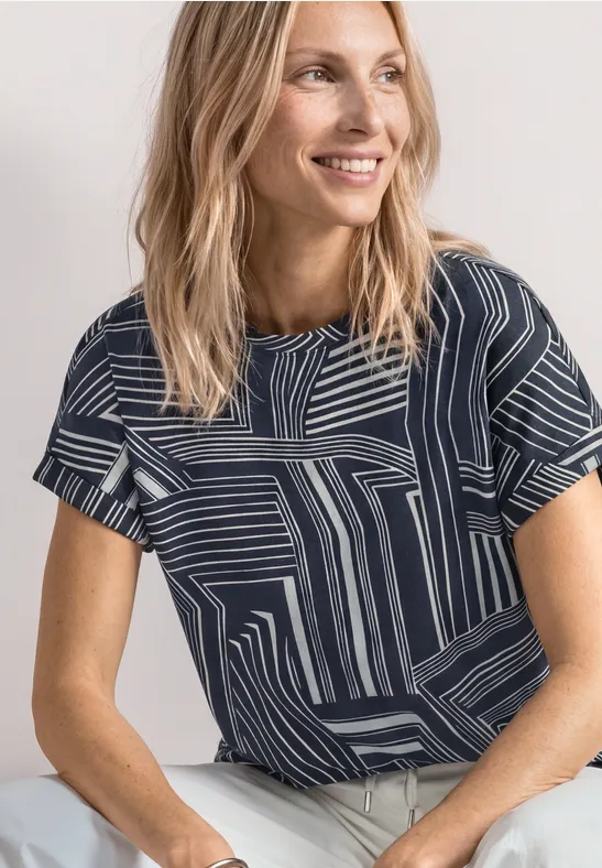 Vrouw draagt marineblauw t-shirt met wit geometrisch patroon en korte mouwen, portretfoto.