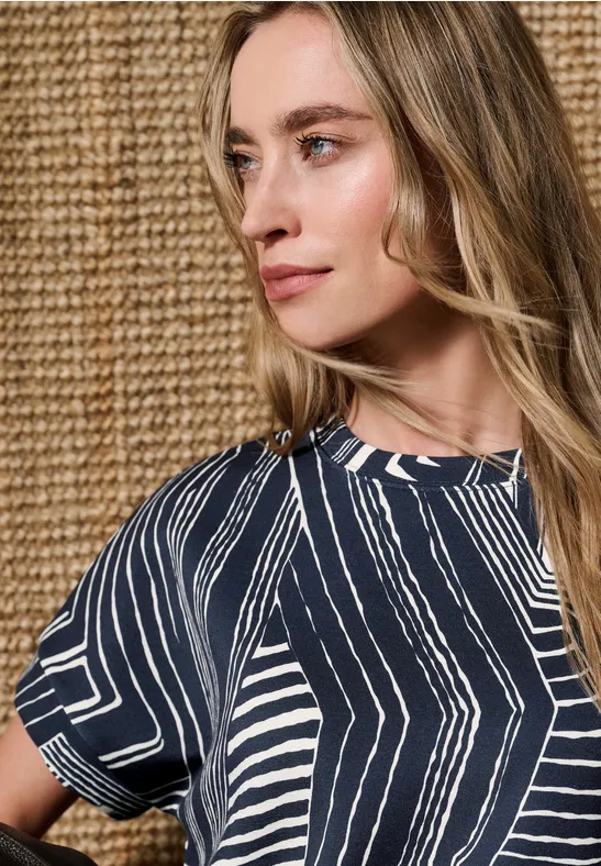 Vrouw met blauw-wit patroonshirt voor een beige gevlochten muur.
