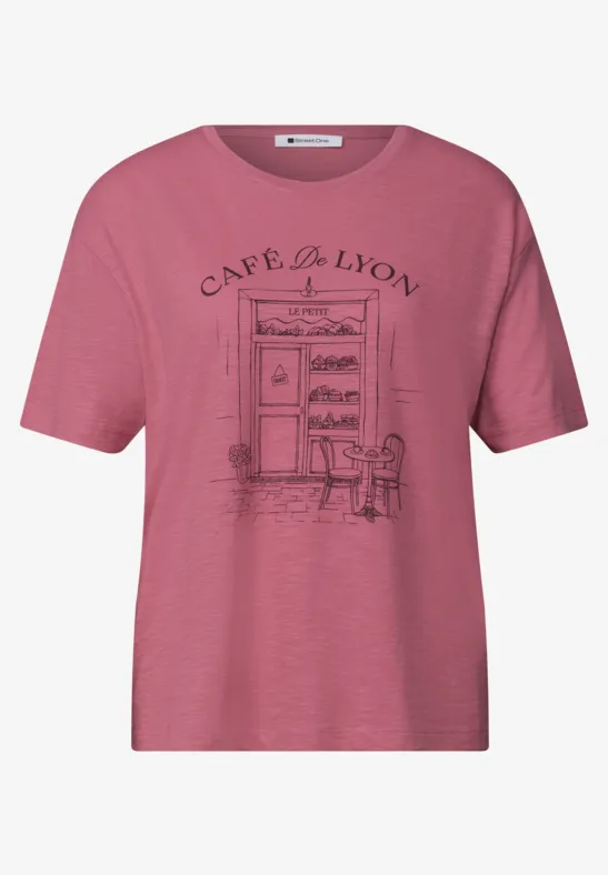 T-shirt rose orné d'un dessin d'entrée de café, deux chaises et l'inscription 'Café du Lion'.