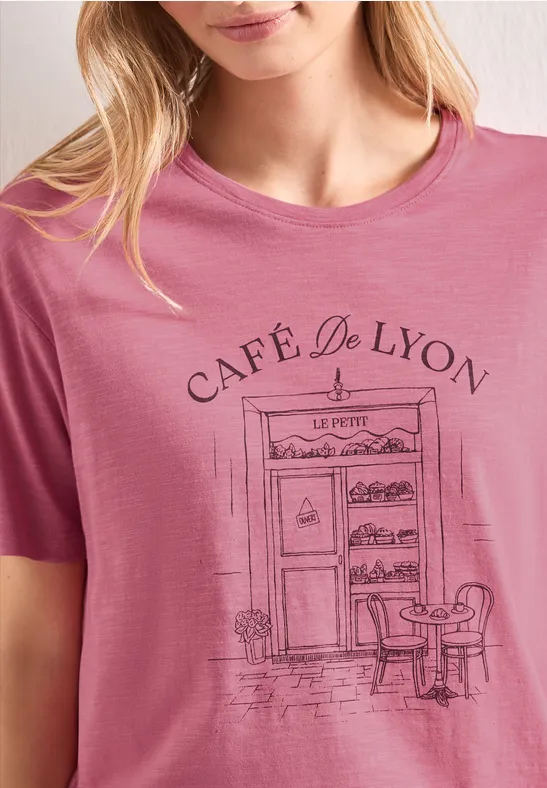 T-shirt rose avec façade dessinée du Café de Lyon, porte, table et chaise.