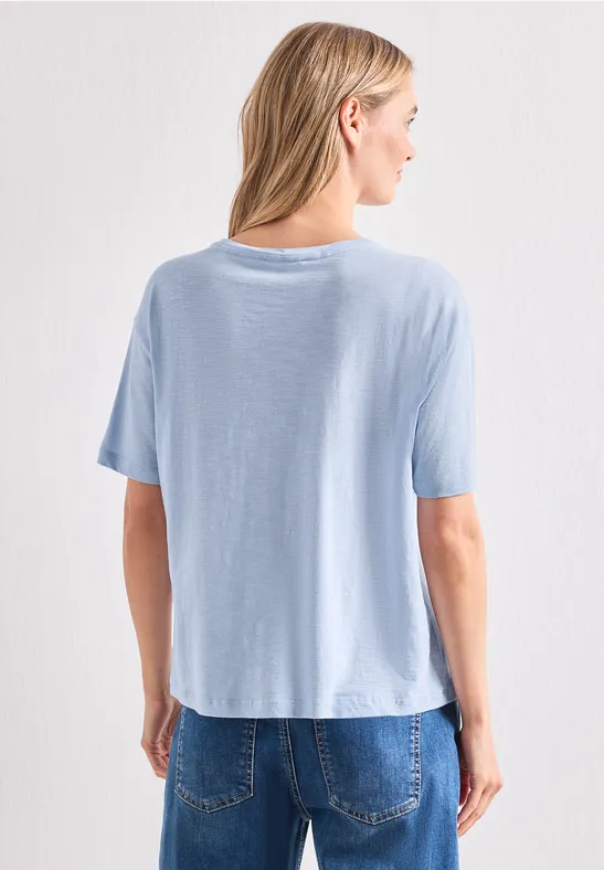 Vue arrière d'une femme portant un t-shirt bleu clair et un jean devant un fond blanc.