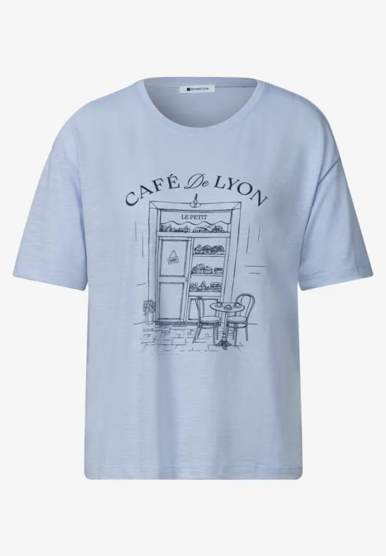 T-shirt bleu clair avec motif Café de Lyon dessiné, façade, table et chaises en esquisse noire.