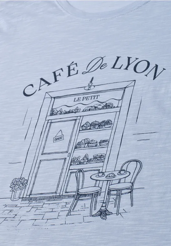 Dessin sur T-shirt: devanture du 'Café De Lyon' avec vitrine de pâtisseries, table et chaises.