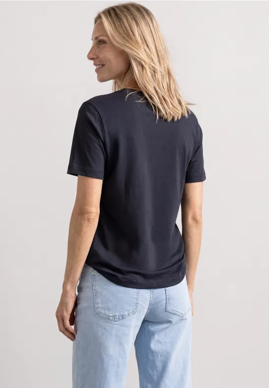 Rückansicht einer Frau in schwarzem T-Shirt und hellblauen Jeans, sie schaut lächelnd zur Seite.