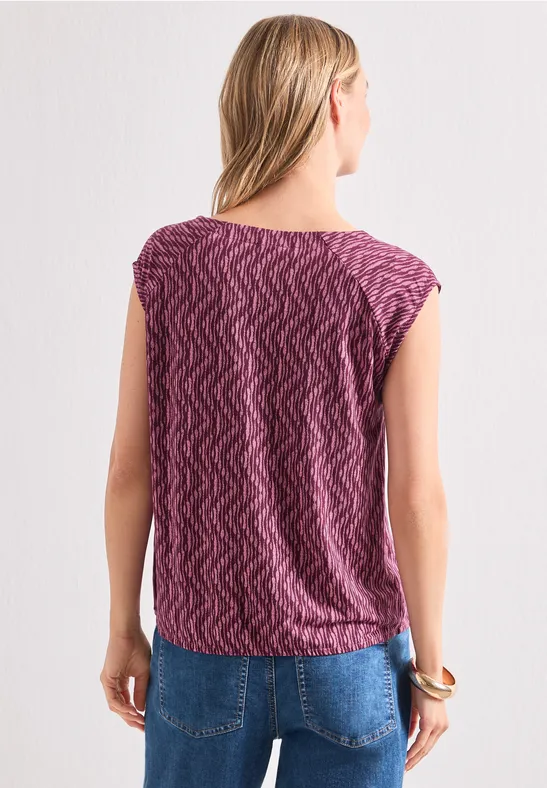 Vrouw van achteren met een paarse top met patroon en een blauwe spijkerbroek.