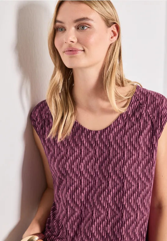 Vrouw tegen witte muur draagt paars shirt met zigzagpatroon