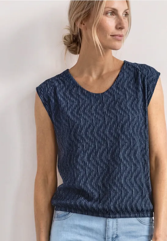 Vrouw met opgestoken haar draagt een mouwloos donkerblauw topje met golvend patroon.