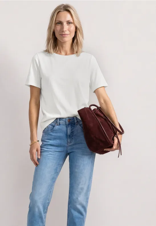 Frau in weißem T-Shirt und blauen Jeans, lässig mit brauner Lederhandtasche.