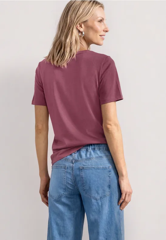 Vrouw van achteren in een paarse t-shirt en blauwe spijkerbroek.