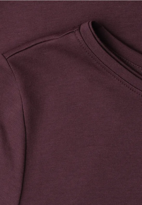 Close-up van een bordeauxrode T-shirt met ronde hals en ingezette mouw.