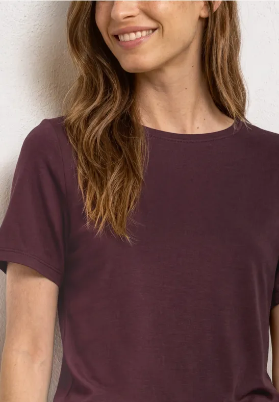 Een vrouw draagt een effen t-shirt met korte mouwen in donkerpaars.