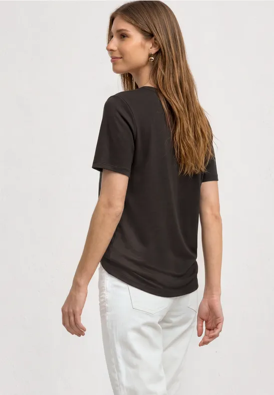 Frau von hinten in schwarzem T-Shirt und weißen Hosen vor weißem Hintergrund.