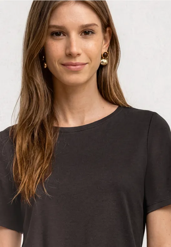 Junge Frau mit langem Haar trägt ein schlichtes dunkelgraues T-Shirt.