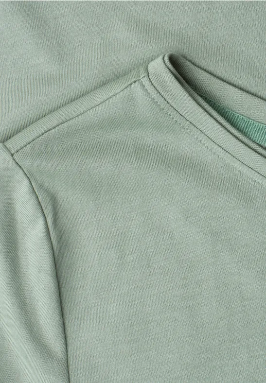 Close-up van een lichtgroen T-shirt met ronde hals en schoudernaden.
