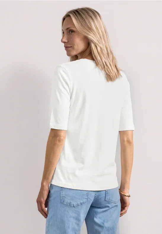 Rückansicht einer Frau mit schulterlangem blondem Haar, weißem Halbarmshirt und blauen Jeans.