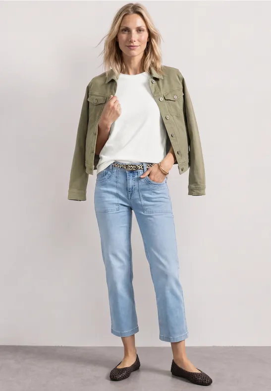 Frau in weißem T-Shirt, Jeans, grüner Jacke und flachen schwarzen Schuhen.