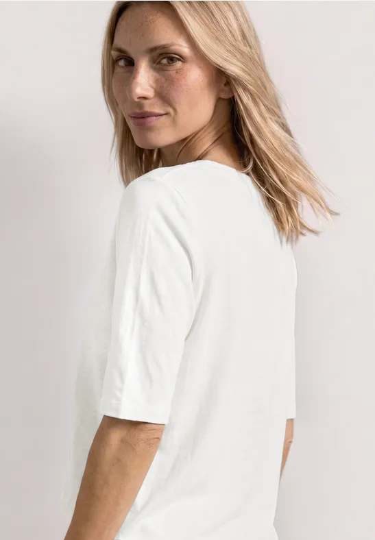Seitlich abgebildete Person mit halblangem blondem Haar trägt ein schlichtes weißes T-Shirt.