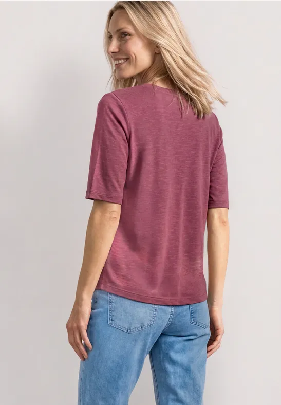 Vrouw van achteren in een roze T-shirt met korte mouwen en een lichtblauwe spijkerbroek.