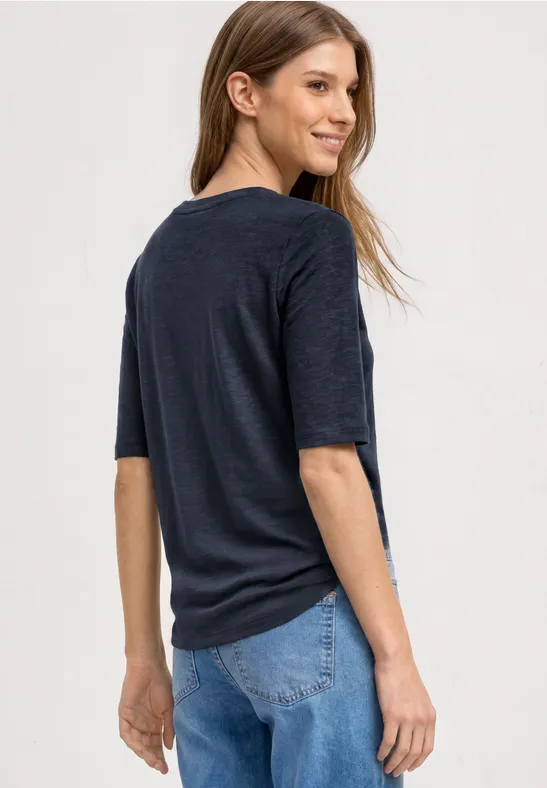Junge Frau in dunklem T-Shirt und blauer Jeans blickt über die Schulter.