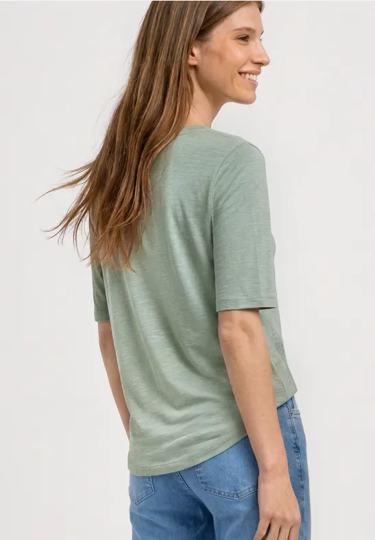 Eine Frau von hinten trägt ein hellgrünes Shirt und blaue Jeans.