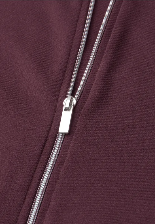 Close-up van een zilverkleurige rits op bordeauxrode stof.