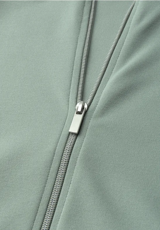 Nahaufnahme eines salbeigrünen Kleidungsstücks mit einem silbernen Reißverschluss.