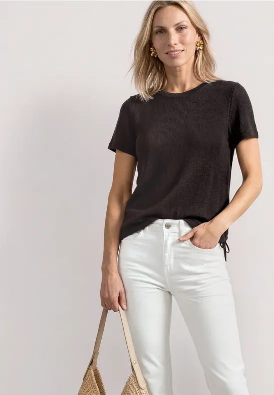 Vrouw in zwart T-shirt en witte spijkerbroek met een beige tas.