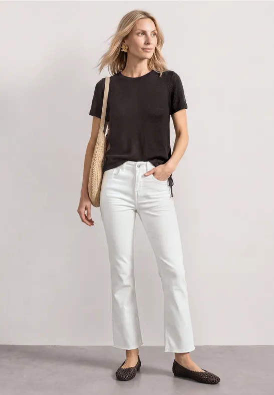 Persoon in casual outfit: zwart t-shirt, witte jeans, zwarte ballerina's en een beige tas.