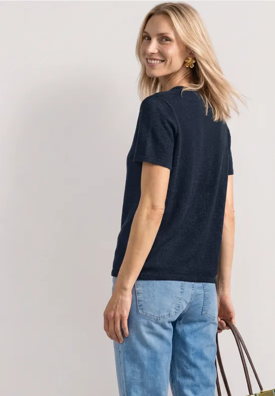 Een vrouw van achteren draagt een donkerblauw shirt, lichte spijkerbroek en houdt een bruine handtas vast.