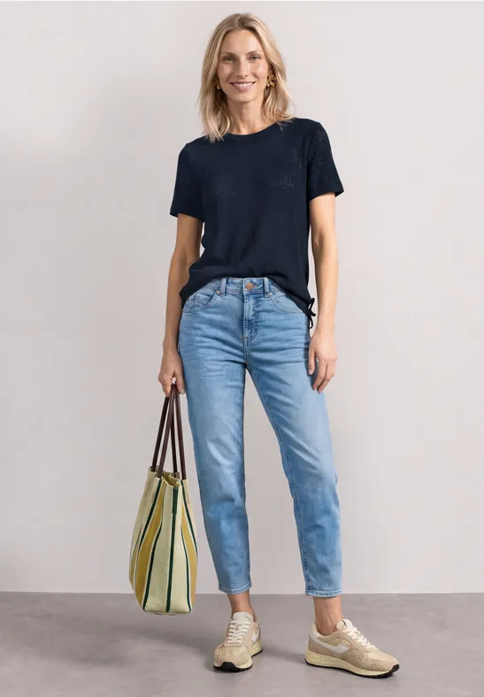 Vrouw draagt zwart T-shirt, lichte jeans, witte sneakers en houdt een groen-geel gestreepte tas vast