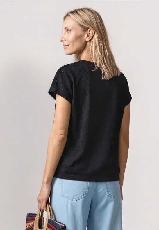 Frau von hinten in schwarzem T-Shirt und hellblauen Jeans, stehend und Tasche in der Hand.
