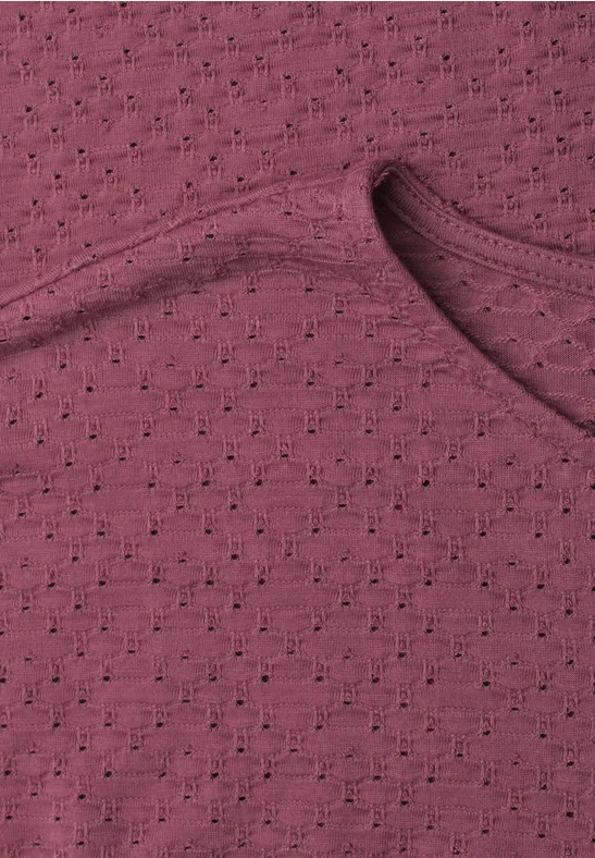 Nahaufnahme eines bordeauxfarbenen, leicht durchlöcherten Strickoberteils mit Rundhalsausschnitt.