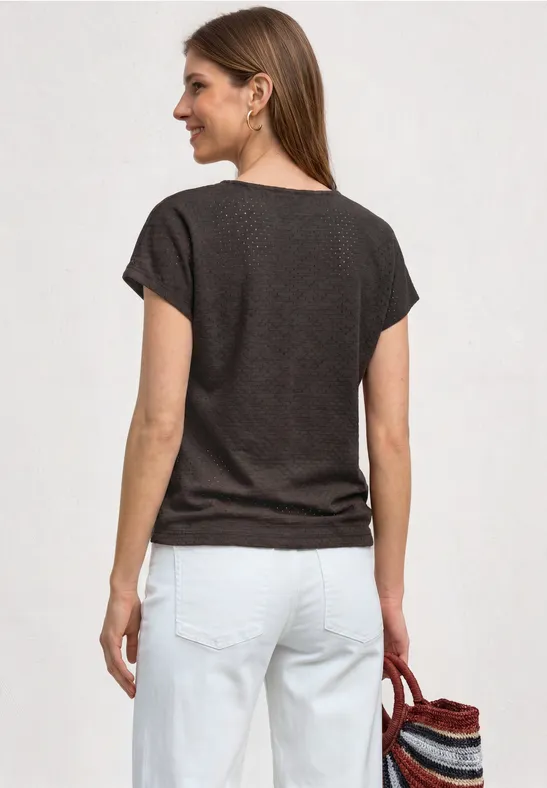 Frau von hinten in dunkelbraunem T-Shirt, weißer Hose, hält bunten Strohkorb.