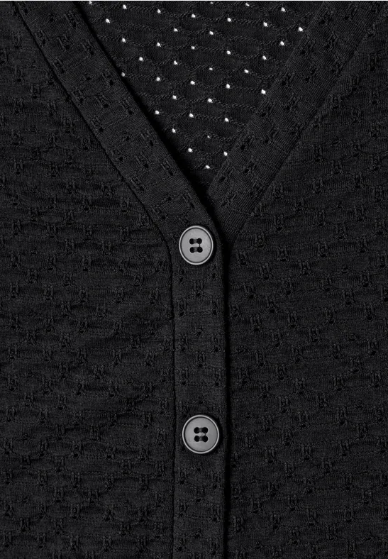 Cardigan noir en maille, encolure en V, deux boutons et motif discret, porté sur un top à pois.