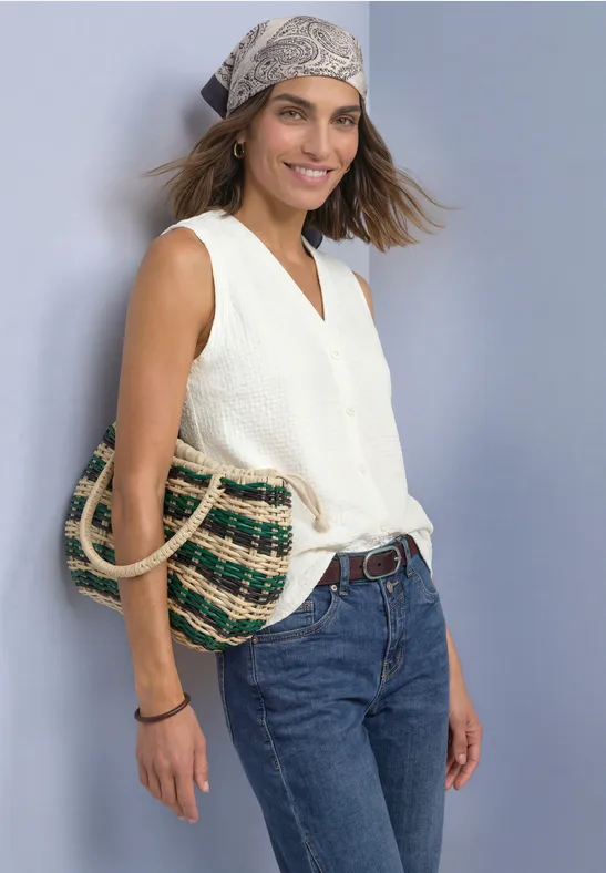 Frau mit weißem Top, Jeans und Kopftuch, lächelnd und mit geflochtener Tasche.