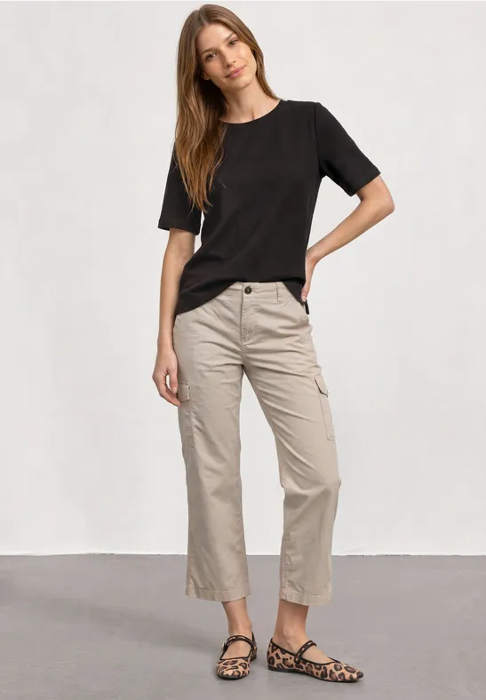 Vrouw in zwart T-shirt, beige korte broek en leopardprint loafers voor een lichte achtergrond.