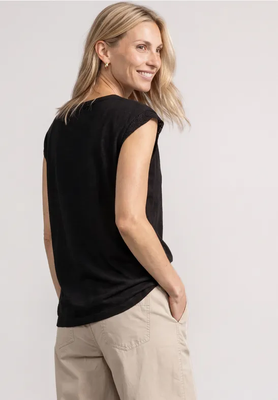 Zijaanzicht van een glimlachende vrouw in een zwart shirt en beige broek, handen in de zakken.