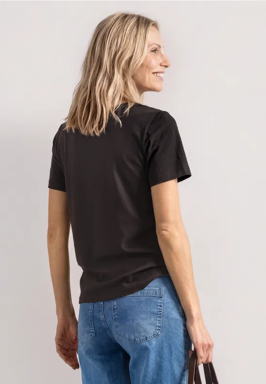 Femme vue de dos portant un t-shirt noir et un jean bleu, cheveux blonds, sur fond clair.