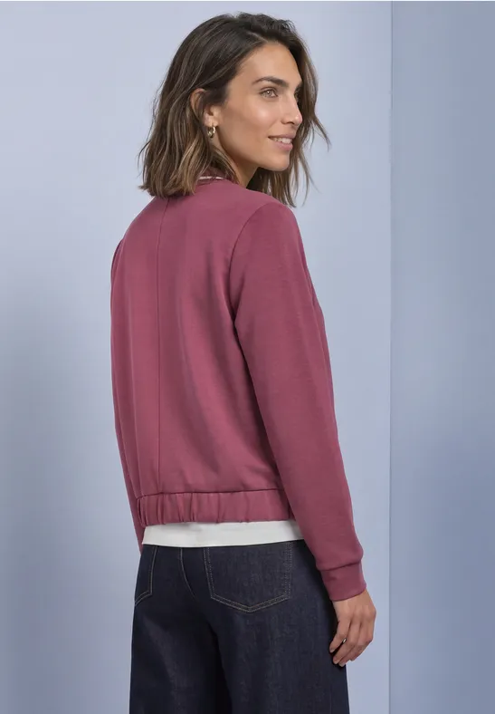 Frau im Profil trägt pinken Pullover und Jeans, blickt über die Schulter.