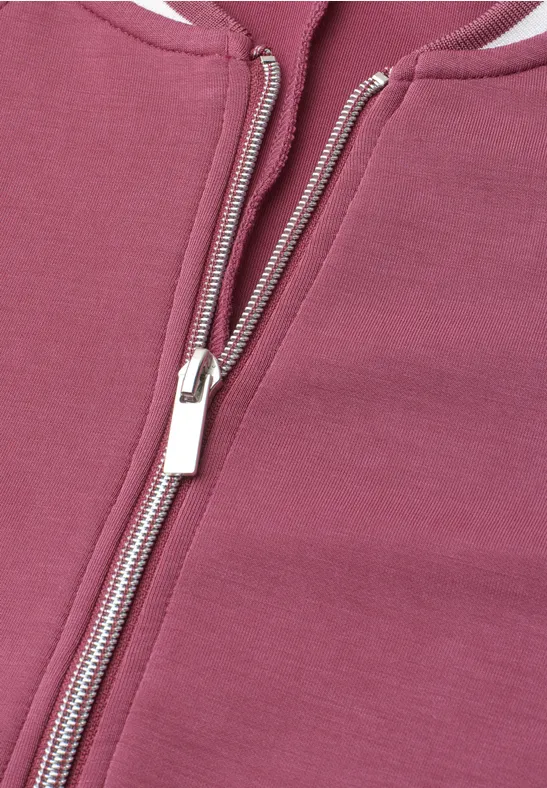Nahaufnahme eines Reißverschlusses an einem rosa bis burgunderfarbenen Kleidungsstück.