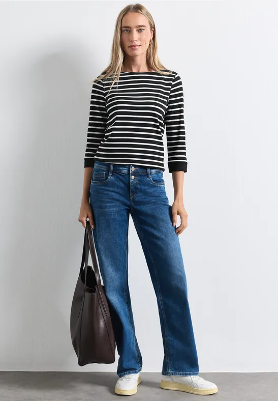 Frau mit schwarz-weiß gestreiftem Shirt, blauen Jeans und großer Tasche.