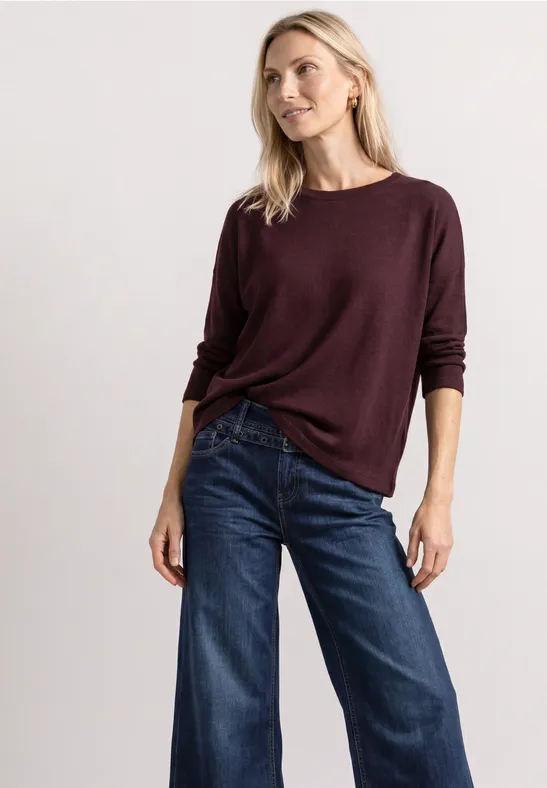 Frau trägt bordeauxroten Pullover und weite Jeans.