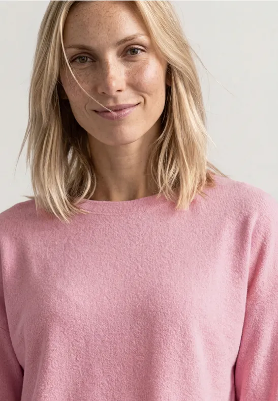 Uśmiechnięta blondynka w różowym swetrze na neutralnym tle.