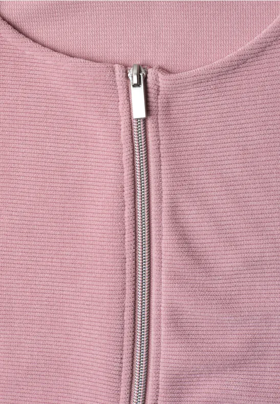Nahaufnahme eines rosa Rippstrick-Oberteils mit silbernem Reißverschluss und rundem Ausschnitt.
