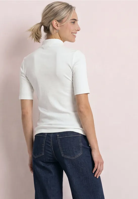 Frau von hinten trägt weißes Kurzarmshirt und blaue Jeans vor rosa Hintergrund.